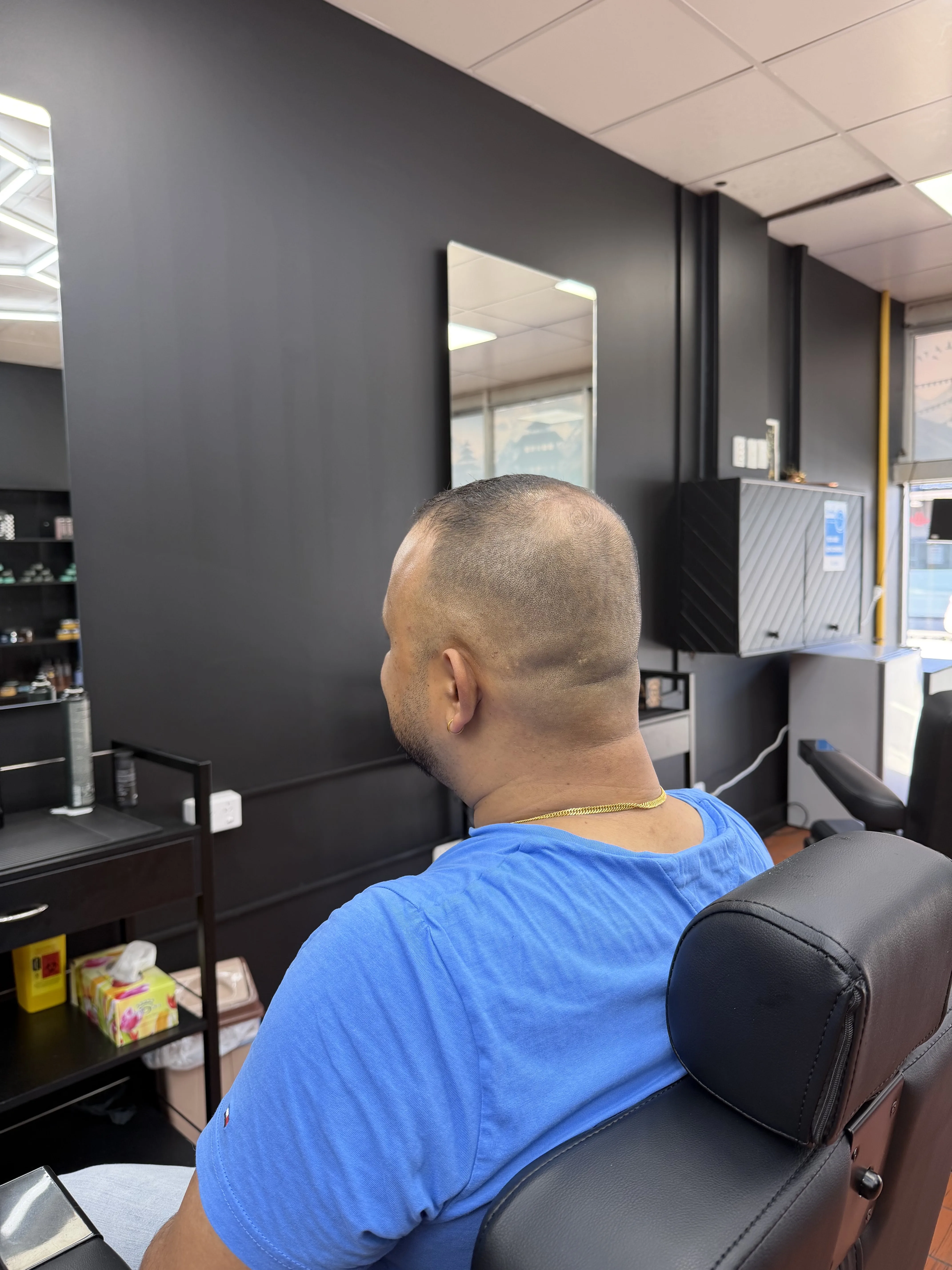Client mid-cut inside Coburg Hair Studio — black feature wall, LED mirror, product shelving